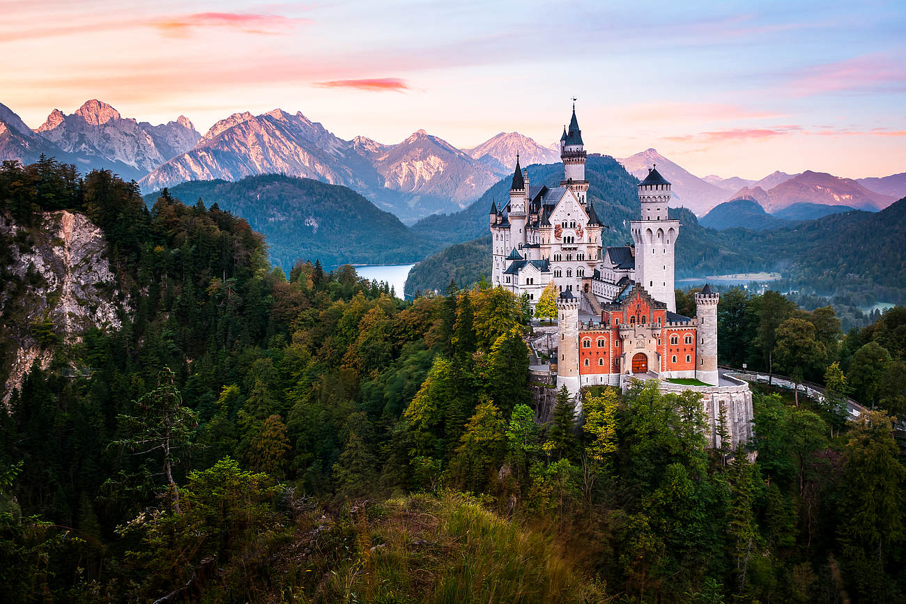 Blick auf das berühmte Schloss Neuschwanstein im Allgäu umgeben von Bäumen und Bergen